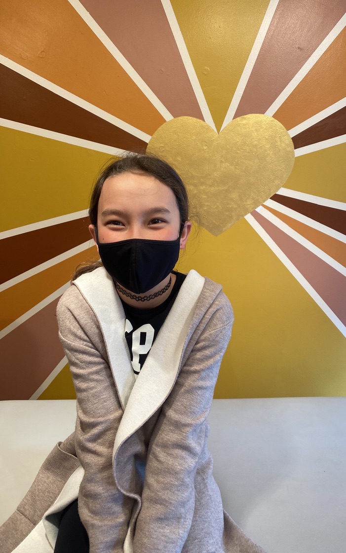 Child smiling in front of the Fabulous by Juliette sunburst wall with a gold heart